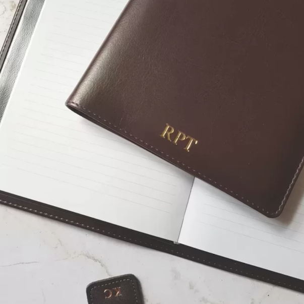 Brown vegan leather notebook personalised with gold initials. The white lined paper inside the notebook is shown.