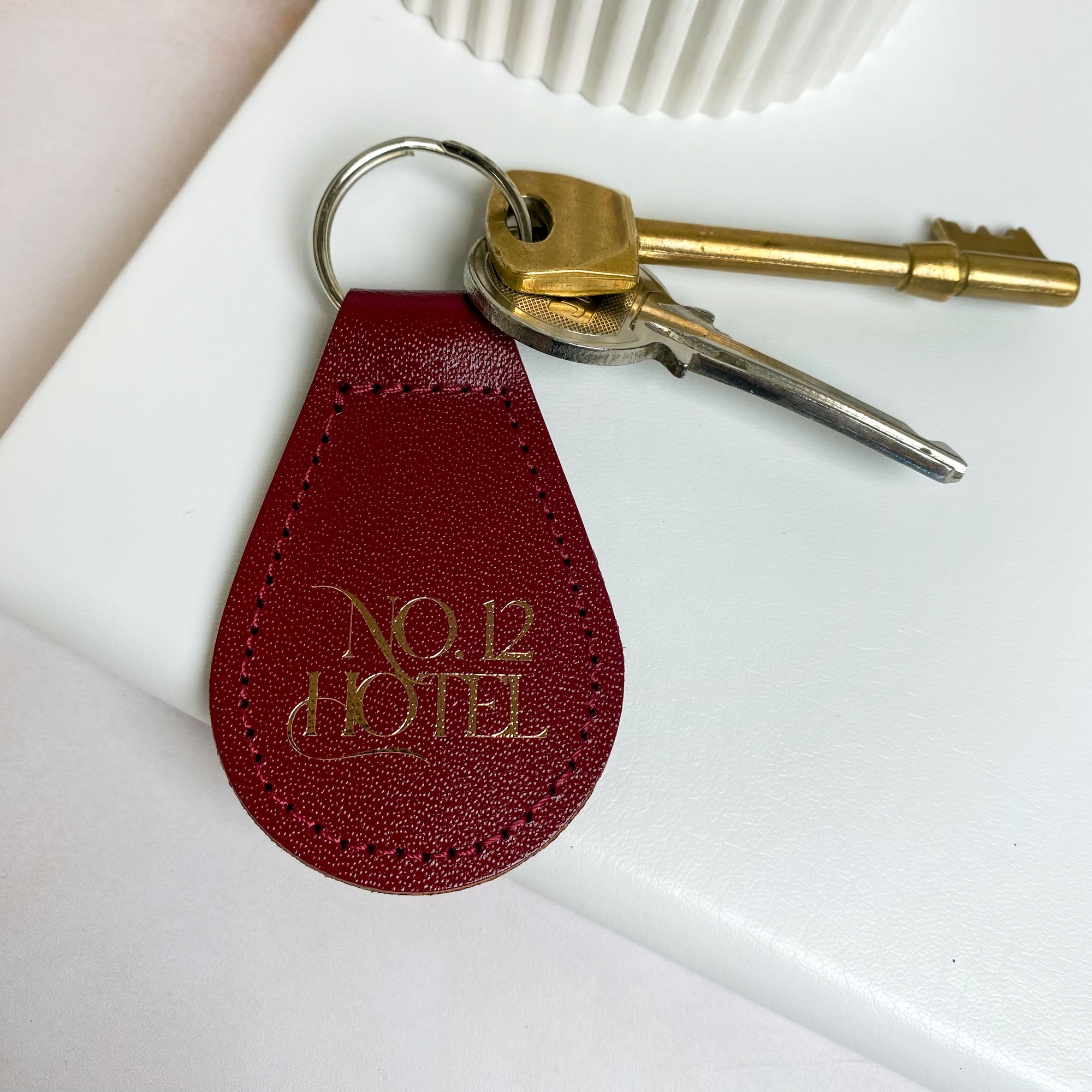 Branded burgundy leather keyring with gold business logo, silver split ring, and two keys attached.